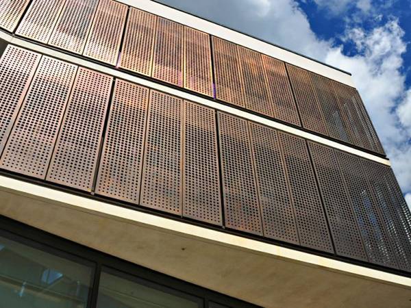 Perforated copper sheets are installed as building cladding.