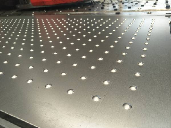 A machine is producing custom orders of decorative perforated metal sheet.