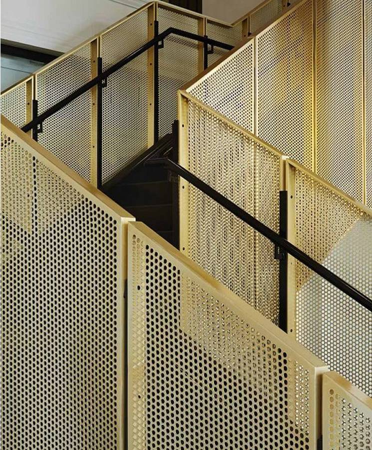 Interior stair railing designed with brass perforated metal panels.