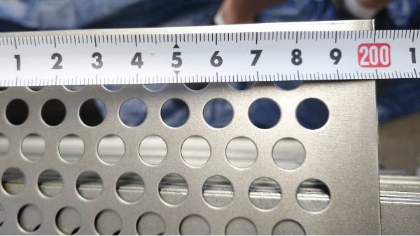 A ruler is used to test the width of the perforated metal sheet.